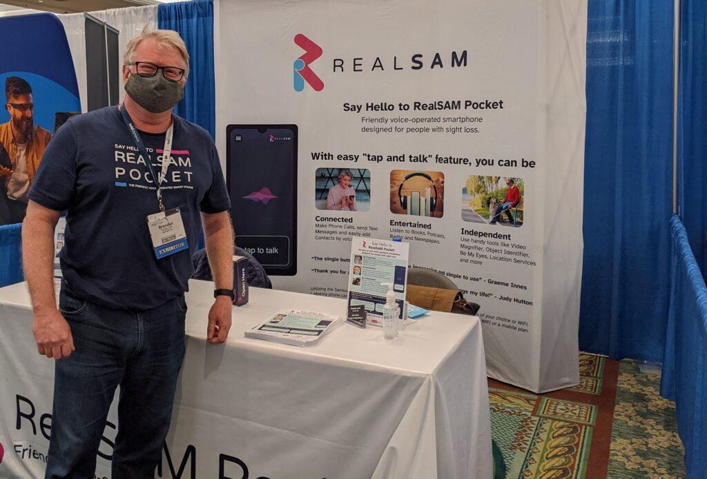 Brendan Lewis is smiling on the background of the RealSAM Pocket booth at ATIA 2022