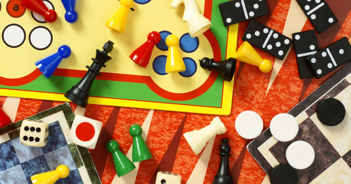 An assortment of classic games represented by their game boards and game pieces strewn about. Games include Chess, Checkers, Dominos, Trouble, etc. – 5 Accessible Games for Holiday Fun